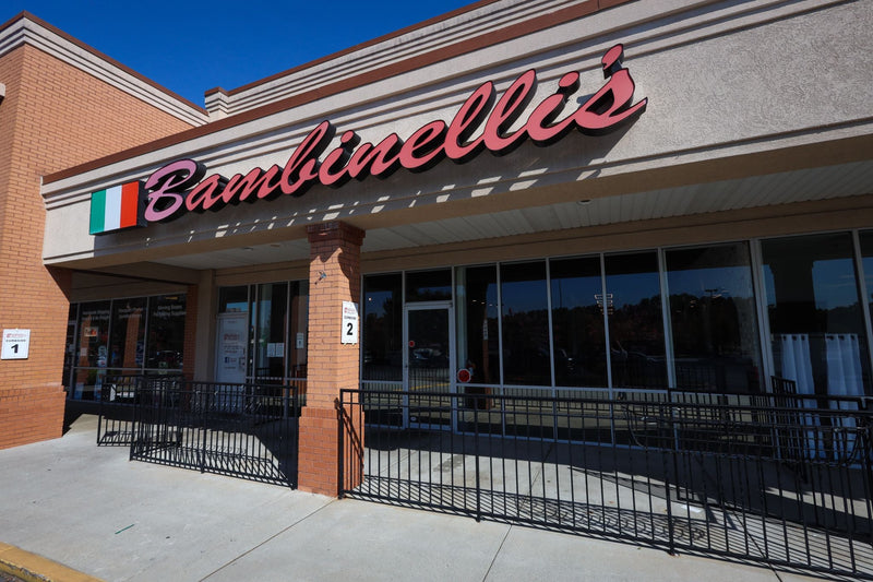 Exterior of Bambinelli’s Italian Restaurant in Lilburn, GA, showing the storefront with red signage, Italian flag, and outdoor entrance.